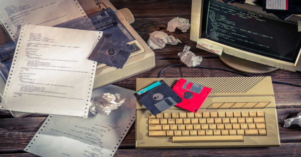 Dot Matrix printer with an old style computer and paper and floppy disks. Legacy ERP