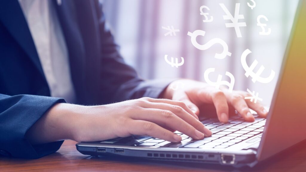 Businessperson typing on a laptop with international currency symbols floating above the keyboard, representing cross-border finance and currency management.
