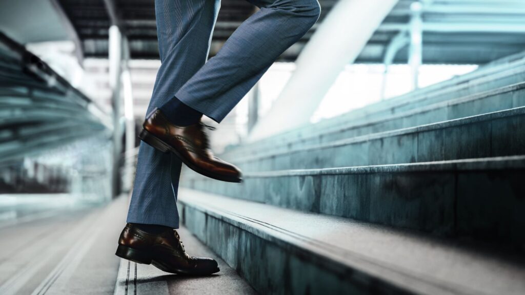 Close-up of a person in business attire stepping up a set of modern marble stairs, symbolizing professional growth, progress, and the journey toward success.