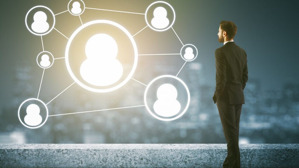 Business professional looking at a glowing digital network of connected people icons, symbolizing knowledge transfer, collaboration, and workforce connectivity in manufacturing and ERP systems.