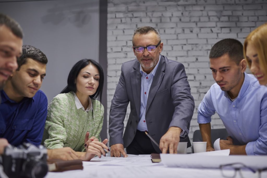 Mature skilled proud CEO wearing eyeglasses with his ERP team