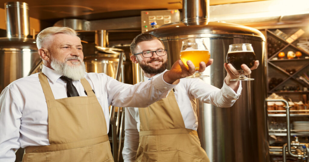 Two brewery specialists standing with glasses of beer and smiling.