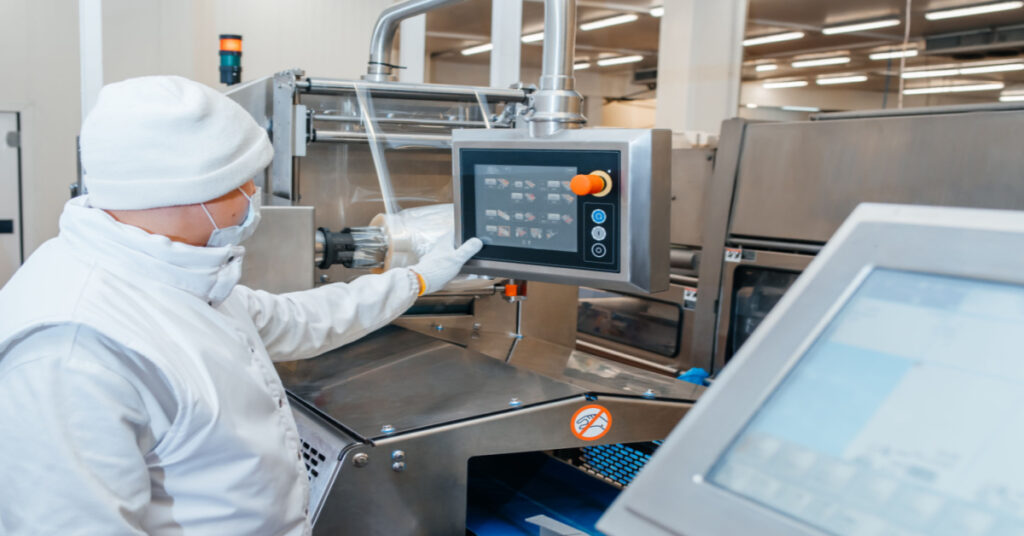 Worker inputting data into computer on meat processing production line.