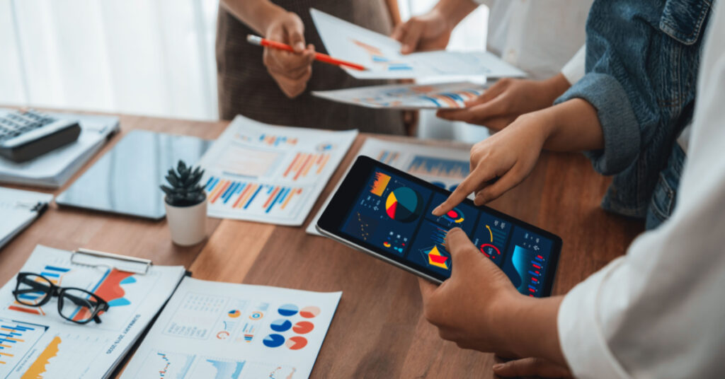 A team of analysts uses BI to analyze financial reports using a tablet with paper on the table to explore the Power BI dashboard screen and gain data insights into the business.