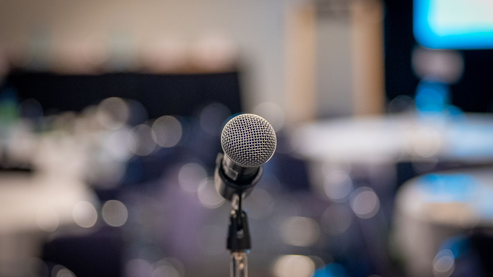Microphone on a stand in focus with a blurred background of a conference room, ready for a session on Business Central Training at a professional event.