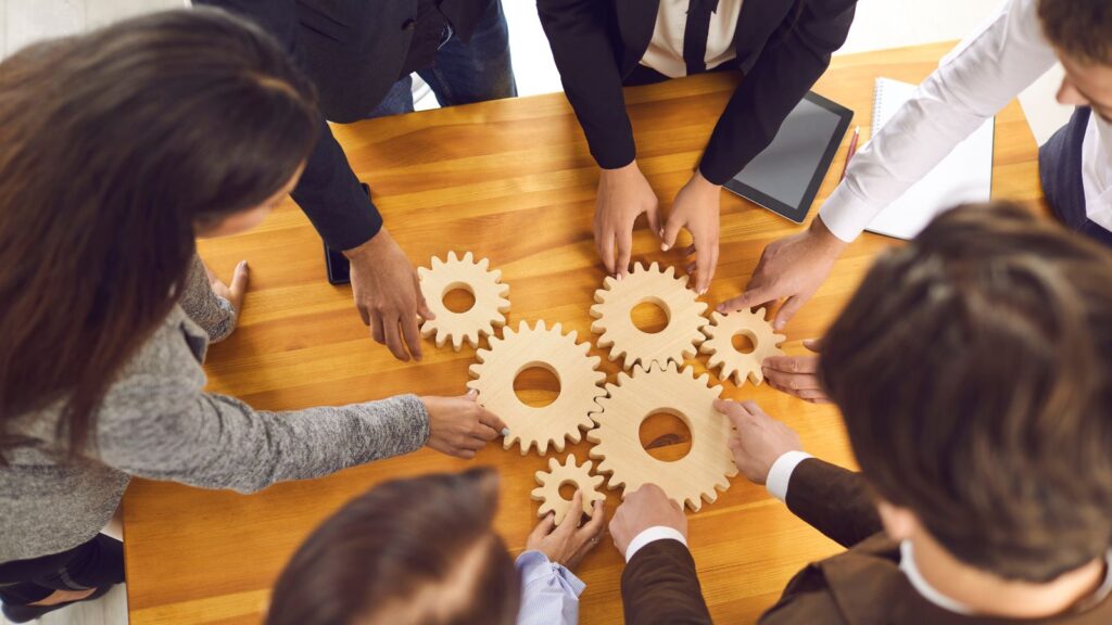 Business Central 2025 Release Wave 1: Enhancing Business Efficiency 1 Team collaborating with interlocking gears on a table, symbolizing improved system integration and operational efficiency with Business Central 2025 Release Wave 1.