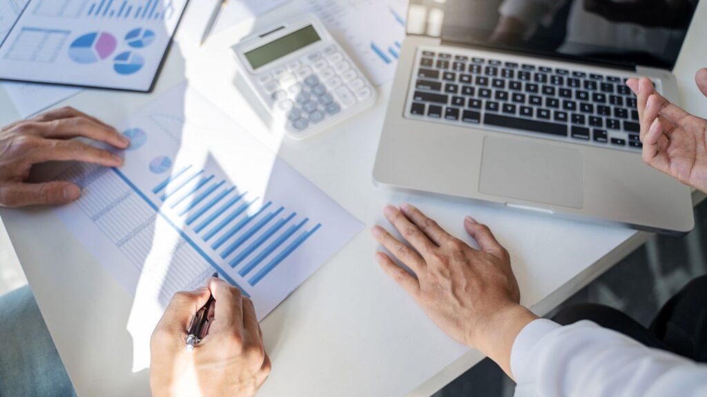 One Size Doesn't Fit All: How Business Central Can Adapt to Any Company's Size 3 Business startup team analyzing printed charts and graphs around a laptop, discussing financial data and performance metrics during a strategy meeting.