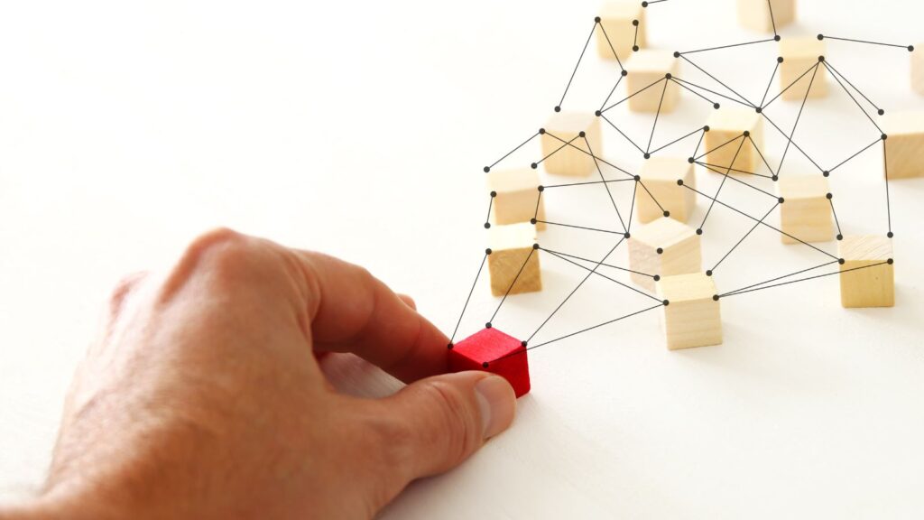 Business Central Multi-Entity Management: Simplifying Global Financial Operations 2 Hand connecting red wooden block to network of linked cubes, representing multi-entity management and organizational connectivity.
