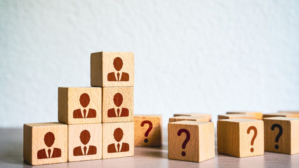 One Size Doesn't Fit All: How Business Central Can Adapt to Any Company's Size 1 Wooden blocks with businessperson icons stacked in a pyramid next to scattered blocks with question marks, symbolizing the concept that "One Size Doesn't Fit All" in ERP solutions and how Business Central adapts to companies of different sizes.