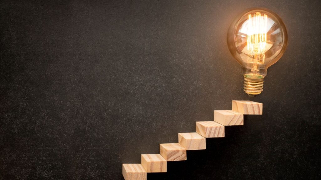 Step-by-Step ERP Migration Roadmap | Move from Legacy ERP to Microsoft Dynamics 365 Business Central 5 Wooden blocks forming steps leading to a glowing lightbulb, symbolizing progress and innovation in an ERP Migration Roadmap to Microsoft Dynamics 365 Business Central.