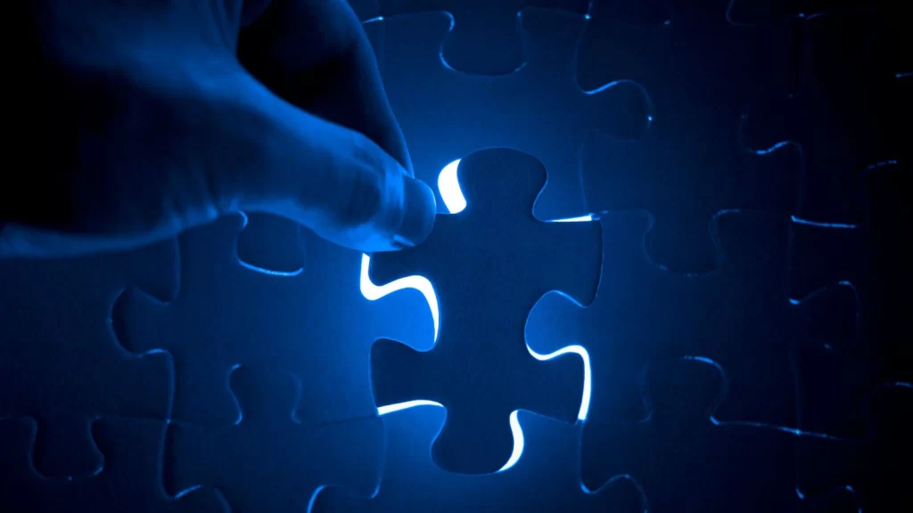 Hand inserting the final puzzle piece into a glowing blue jigsaw, representing completion and solving the missing piece.