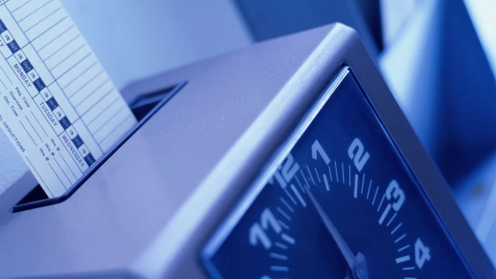 Close-up of a time clock machine with an employee time card inserted, representing labor time tracking and workforce management in a manufacturing environment.